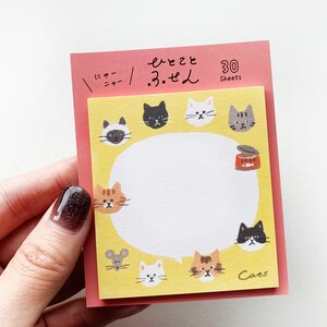 Könnte beinhalten: Ein gelber und rosa Notizblock mit einer Sprechblase und Katzenillustrationen. Der Notizblock hat 30 Blätter und steht unten "Cats". Die Sprechblase hat einen weißen Hintergrund und ist von Katzenköpfen umgeben.