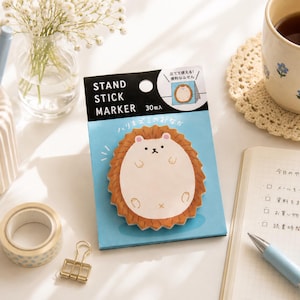 Può includere: Una confezione da 30 foglietti adesivi a forma di riccio con la scritta STAND STICK MARKER. La confezione presenta uno sfondo azzurro con un'illustrazione di un riccio marrone e crema. Il testo include caratteri giapponesi e le parole inglesi.