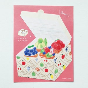 Puede incluir: Tarjeta de felicitación rosa con un diseño de caja blanca, con ilustraciones de tartas de frutas. La caja está abierta, revelando las tartas. La tarjeta tiene el texto "Open!" y texto japonés.