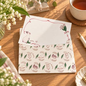 May include: A white stationery card with a red decorative border, a small rabbit illustration, and a lily of the valley sprig, tucked into an envelope featuring a repeating pattern of rabbits, lily of the valley, and the text Return of happiness.