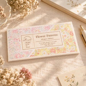 Può includere: Una confezione rettangolare di fogli di carta washi con un motivo floreale nei toni del rosa, giallo e bianco. L'etichetta riporta Flower Patterns, 2designs 16sheets, Risette, Made in Japan, e un testo su regali e affetto.