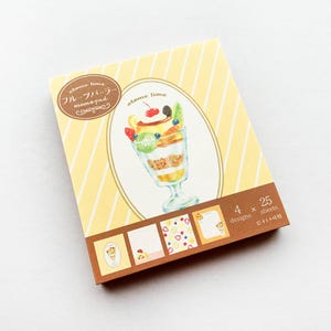 May include: A pack of 100 memo pads with 4 different designs featuring illustrations of fruit parfaits. The memo pads are yellow with brown stripes and the text "stone lime フルーツメモpad" is printed on the front. The back of the pack says "4 x 25 sheets designs"