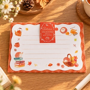 Könnte beinhalten: Ein rechteckiges Briefpapier-Set mit einem weißen, wellenförmig geschnittenen Schreibblatt und orangefarbenen Linien. Das Design zeigt Aquarellillustrationen von Igeln, Herbstblättern, einer Teekanne und Büchern. Ein rotes Etikett trägt die Aufschrift Autumn Letter & Envelope.