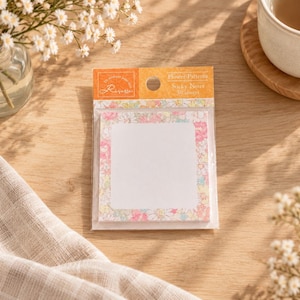 Könnte beinhalten: Eine Packung mit 30 quadratischen Haftnotizen mit einem floralen Randmuster in Rosa-, Gelb- und Blautönen. Die Verpackung ist mit Flower Patterns Sticky Notes 30 sheets und Risette beschriftet. Die Notizen haben eine weiße Mitte zum Schreiben.