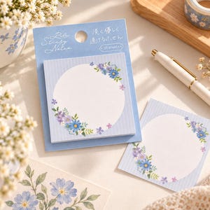 Peut inclure: Un paquet de notes adhésives carrées sur un support bleu avec le texte Pale Sticky Notes et des caractères japonais. Les notes présentent un centre circulaire blanc encadré d'illustrations florales bleues et violettes sur un fond rayé bleu clair.