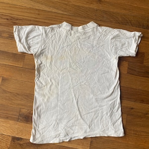 May include: White t-shirt with a faded yellow stain on the front.