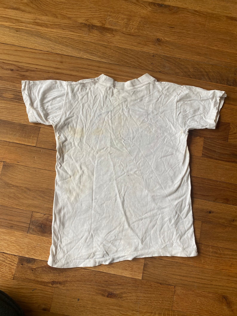 May include: White t-shirt with a faded yellow stain on the front.