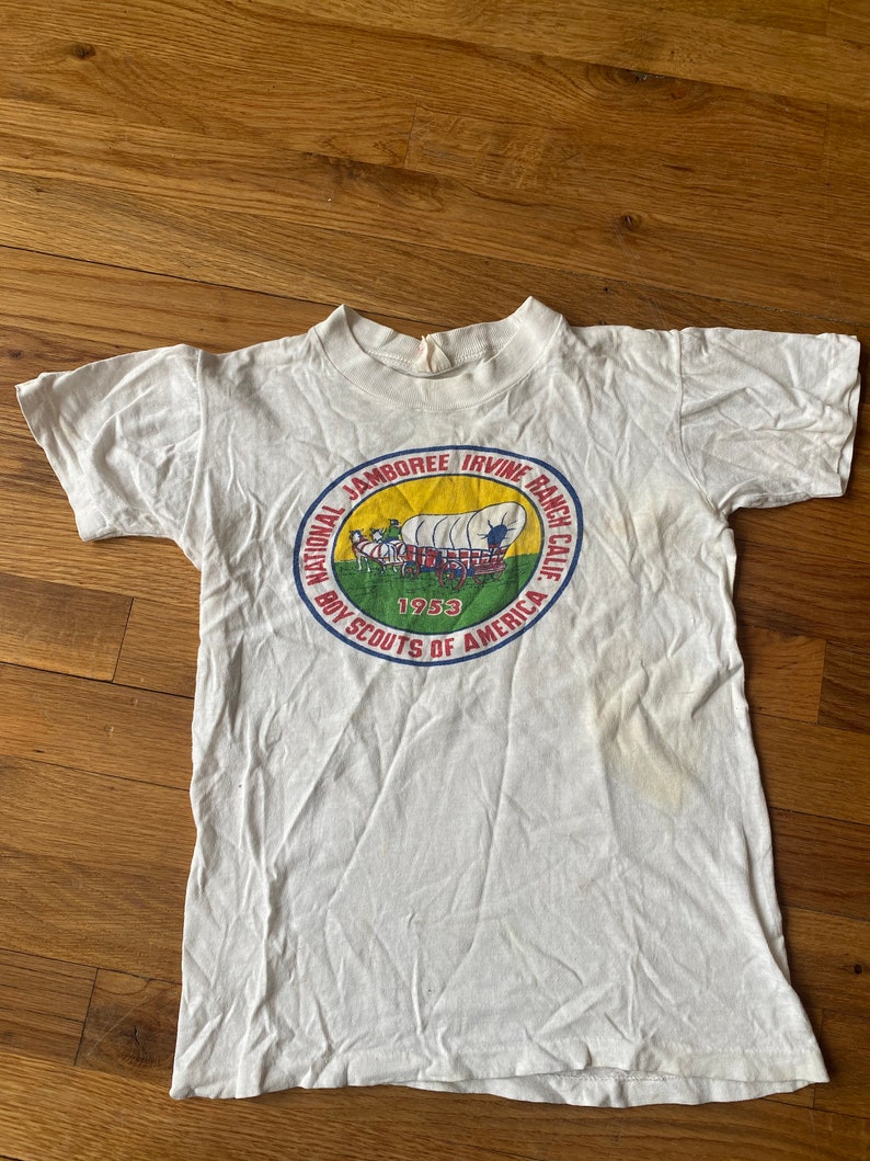 May include: White t-shirt with a circular graphic of a wagon train and the text "National Jamboree Irvine Ranch Calif. Boy Scouts of America 1953"