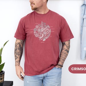 May include: Crimson t-shirt with a grey clockwork design. The graphic features gears and labeled components. The shirt is a solid colour and has short sleeves. The word "CRIMSON" is in a red rectangle.