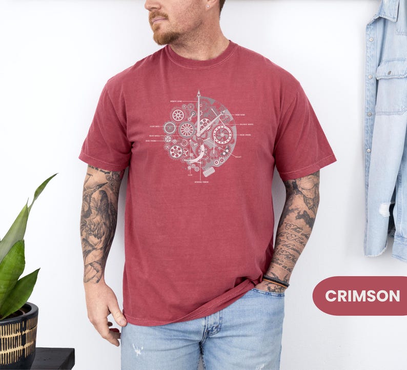 May include: Crimson t-shirt with a grey clockwork design. The graphic features gears and labeled components. The shirt is a solid colour and has short sleeves. The word "CRIMSON" is in a red rectangle.