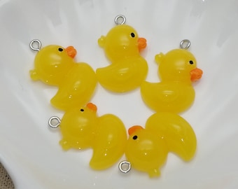 May include: Five yellow rubber duck charms with silver jump rings. The ducks are in a white ceramic bowl.