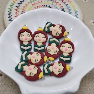 May include: A collection of eight green and maroon resin charms featuring a cartoon girl with a crown. Each charm has a gold loop for attaching to a necklace, bracelet, or other jewellery.