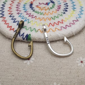 May include: Two silver and bronze fish hook charms with the word "HOPE" engraved on them.