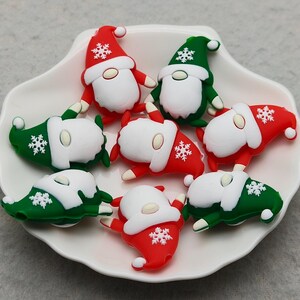 May include: A white, scalloped dish holds several Christmas gnome figurines. The gnomes are red and green with white beards and hats, and snowflake accents. The figurines are arranged on a white plate.