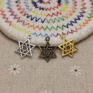 May include: Three metal Star of David charms in silver, bronze, and gold. Each charm features a six-pointed star design with an inner star. The charms are displayed on a white and rainbow-colored surface.