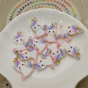 May include: A collection of 10 white unicorn charms with pink, purple, and blue accents. Each charm has a silver loop for attaching to a necklace, bracelet, or other jewelry.