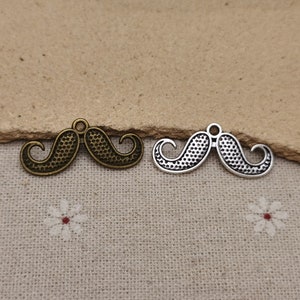 May include: Two metal mustache charms, one in antique gold and one in silver. Both charms have a textured surface and a loop for attaching to a necklace or bracelet.