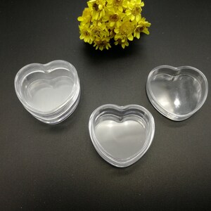 Op de afbeelding: Drie transparante, hartvormige plastic containers. De containers zijn op elkaar gestapeld.