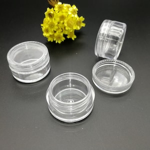 Op de afbeelding: Vier transparante plastic containers met deksels. De containers zijn rond en hebben een gladde, glanzende afwerking. Ze zijn ideaal voor het opbergen van kleine items, zoals sieraden, cosmetica of knutselspullen.