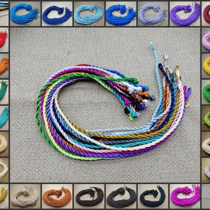 Puede incluir: Una colección de 24 carretes de cordón trenzado de colores. Los cordones están dispuestos en círculo y son de diferentes colores, incluyendo rojo, azul, verde, amarillo, morado y blanco.