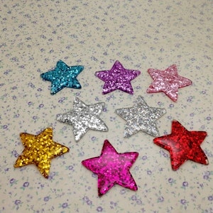 May include: Assortment of eight glitter star embellishments in various colors, including pink, blue, silver, gold, and red. The stars are all the same size and shape, and they have a sparkly finish.