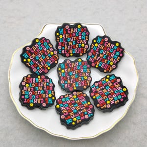 May include: Six black and colorful round buttons with the text "We cannot change the outcome but we can affect the journey" repeated on each button.