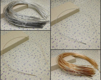 Può includere: Un assortimento di basi per cerchietti in metallo argentato, dorato e ramato. L'immagine mostra cerchietti singoli e mazzi, ideali per il fai-da-te o la creazione di gioielli. I cerchietti sono esposti su una superficie a fantasia floreale.