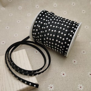May include: A spool of black leather cord with silver studs. The cord is rolled up and the end is hanging down.
