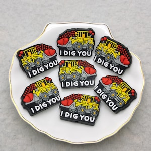 May include: Seven yellow and black toy construction vehicles with red hearts and the text "I DIG YOU" on each.
