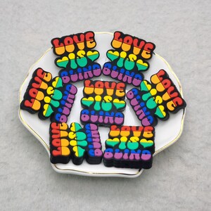 May include: Eight rainbow-colored charms with the text "Love is Blind" in a white and gold decorative dish.