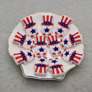 May include: A collection of 12 red, white, and blue gnome-themed silicone charms. Each charm features a gnome wearing a red, white, and blue hat with a white beard and a star on the hat.