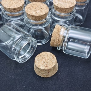 May include: A group of small, clear glass jars with cork lids. The jars are arranged on a black surface.
