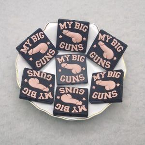 May include: Seven black square patches with the text "My Big Guns" and a cartoon image of a gun. The patches are arranged in a circle on a white plate.