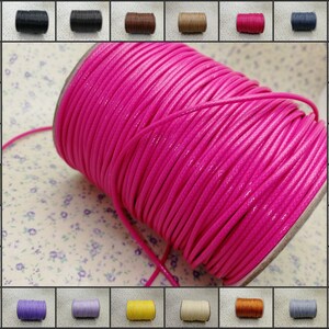 Könnte beinhalten: Eine Spule mit leuchtend pinkfarbenem gewachstem Schnüren, im Hintergrund sind verschiedene andere Farben von Schnüren zu sehen.