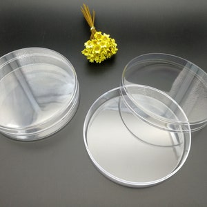 Op de afbeelding: Drie ronde, transparante plastic containers, waarvan er één op de andere gestapeld is. De containers zijn leeg en hebben een glad, glanzend oppervlak.