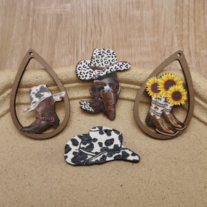 May include: Five wooden cutouts with different designs. The cutouts feature a cowboy boot with a hat, a cowboy hat with a cow print, a pair of cowboy boots with sunflowers, a cowboy boot with a hat, and a cowboy hat with a cow print.