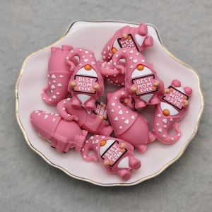 May include: A collection of pink gnome-shaped resin charms with white hearts and the text "Best Mom Ever" on each charm.
