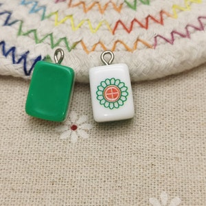 Peut inclure: Deux tuiles de mahjong en c&eacute;ramique verte et blanche avec des boucles argent&eacute;es. La tuile verte est vide et la tuile blanche a un motif de fleur rouge et verte.