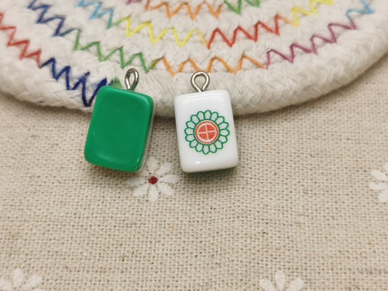 Peut inclure: Deux tuiles de mahjong en c&eacute;ramique verte et blanche avec des boucles argent&eacute;es. La tuile verte est vide et la tuile blanche a un motif de fleur rouge et verte.