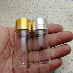 May include: Two glass bottles with clear glass bodies and metal caps. The bottle on the left has a gold cap, and the bottle on the right has a silver cap.