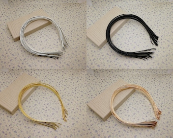 Può includere: Un set di dieci cerchietti per capelli in metallo argento, nero e oro. I cerchietti sono impilati uno sopra l'altro e disposti in cerchio.