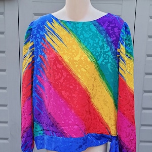May include: A long-sleeved blouse with a rainbow pattern. The blouse has a tie at the waist and a blue trim.