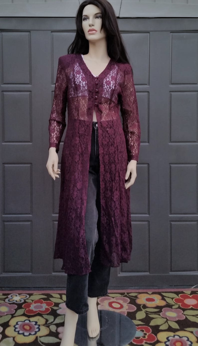 Puede incluir: Una larga chaqueta de encaje color burdeos con cierre de botones y mangas largas. La chaqueta es transparente y tiene un patr&oacute;n floral.