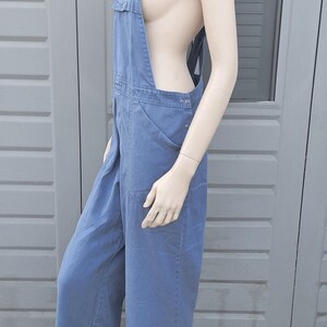 Op de afbeelding: Een blauwe denim overall met wijde pijpen en verstelbare schouderbanden. De overall is gemaakt van een stevige, duurzame stof en heeft een klassieke, utilitaire stijl.