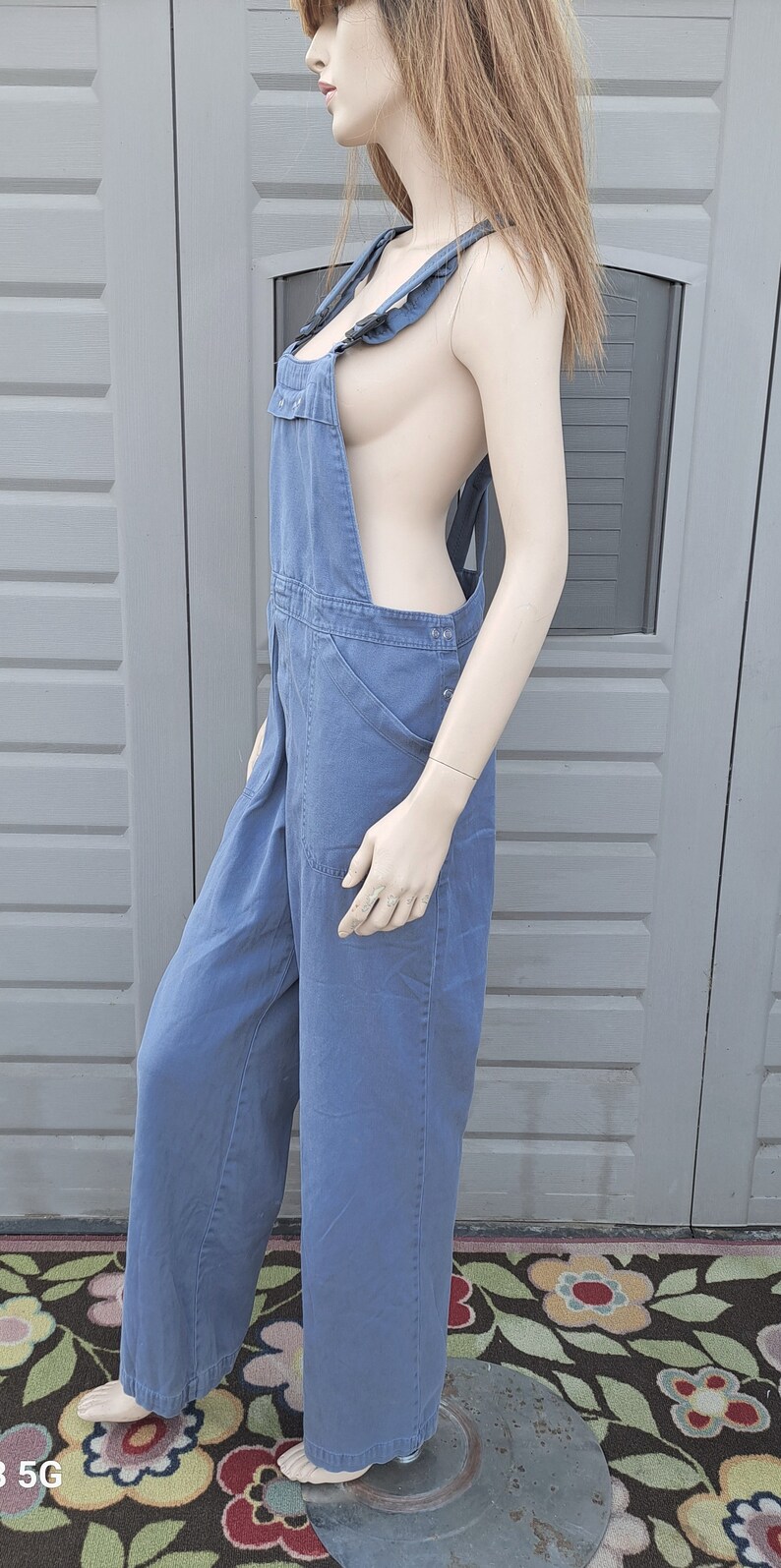 Op de afbeelding: Een blauwe denim overall met wijde pijpen en verstelbare schouderbanden. De overall is gemaakt van een stevige, duurzame stof en heeft een klassieke, utilitaire stijl.