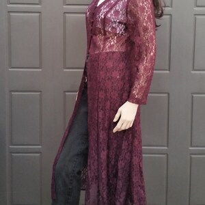 Puede incluir: Un c&aacute;rdigan largo de encaje color burdeos con cuello en V y mangas largas. El c&aacute;rdigan es transparente y tiene un delicado estampado floral. Se lleva sobre un top blanco sin mangas y unos vaqueros negros.