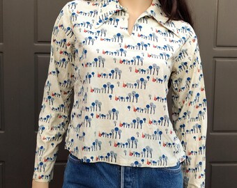 May include: A white long-sleeved shirt with a blue and red print of trees. The shirt has a collared neckline and a slightly cropped length.
