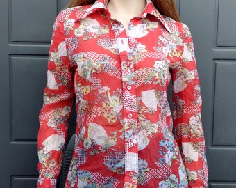 May include: A red sheer button-down shirt with a colorful floral and geometric print. The shirt has long sleeves and a collared neckline.