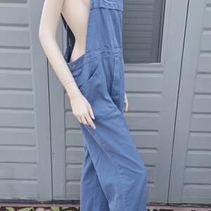 Op de afbeelding: Een blauwe denim overall met zwarte banden. De overall heeft een losse pasvorm en is gemaakt van een duurzame stof.