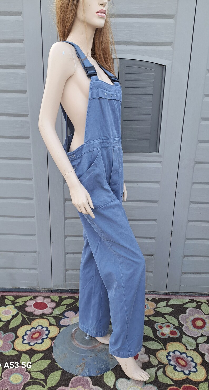 Op de afbeelding: Een blauwe denim overall met zwarte banden. De overall heeft een losse pasvorm en is gemaakt van een duurzame stof.